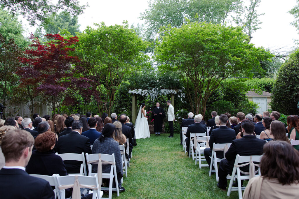 Audience watch bride and groom wed in a garden outside Tuckahoe Women's Club.